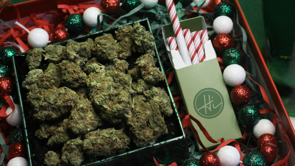 A holiday-themed gift box filled with cannabis flower and candy cane-striped pre-rolls, surrounded by festive red, green, and white decorations.