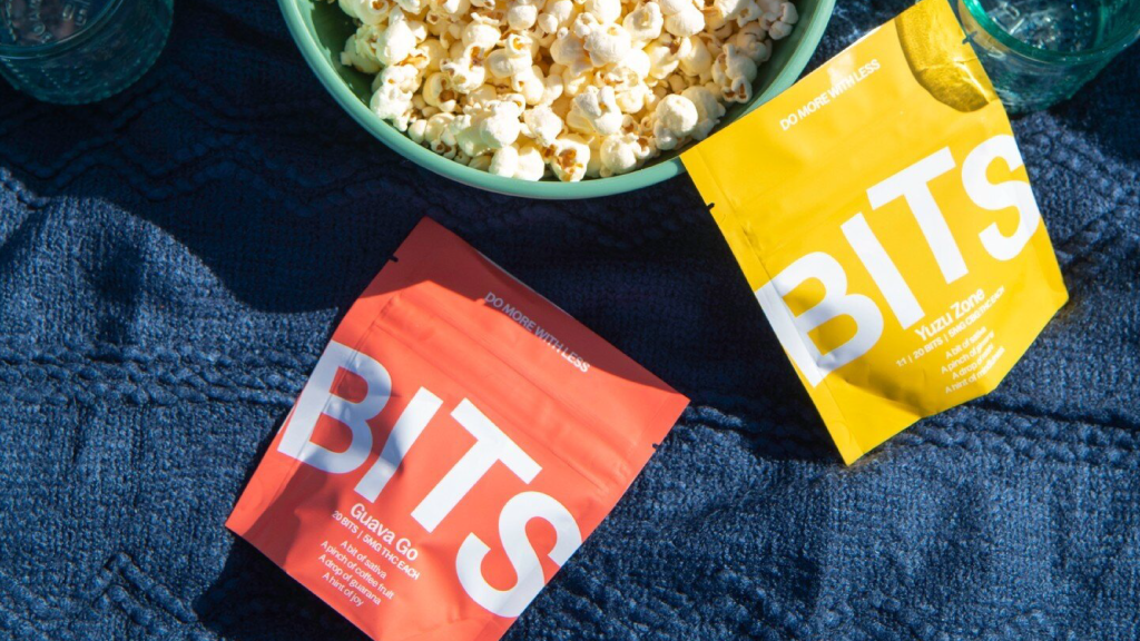 Bits edibles Dragonfruit and Yuzu Zone gummies displayed on a picnic blanket next to a bowl of popcorn, showcasing their colorful and functional cannabis packaging.