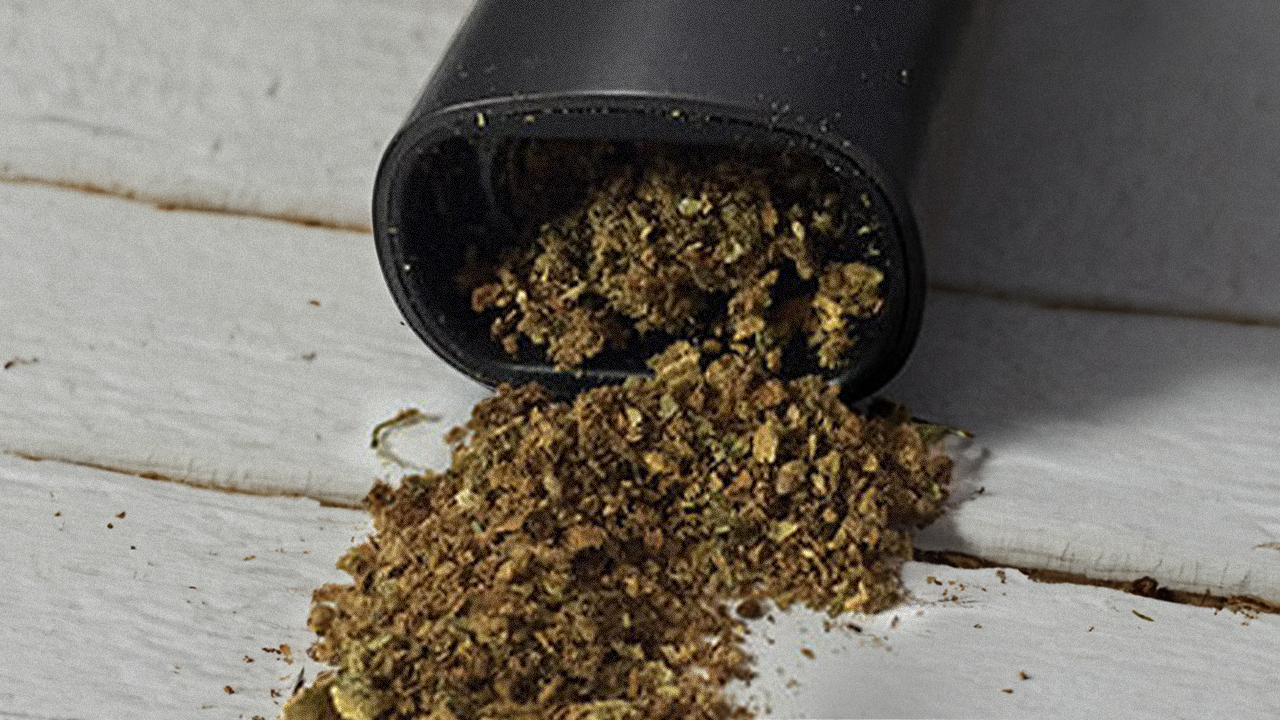 Ground ABV cannabis spilling out of a dry herb vaporizer onto a white wooden surface.