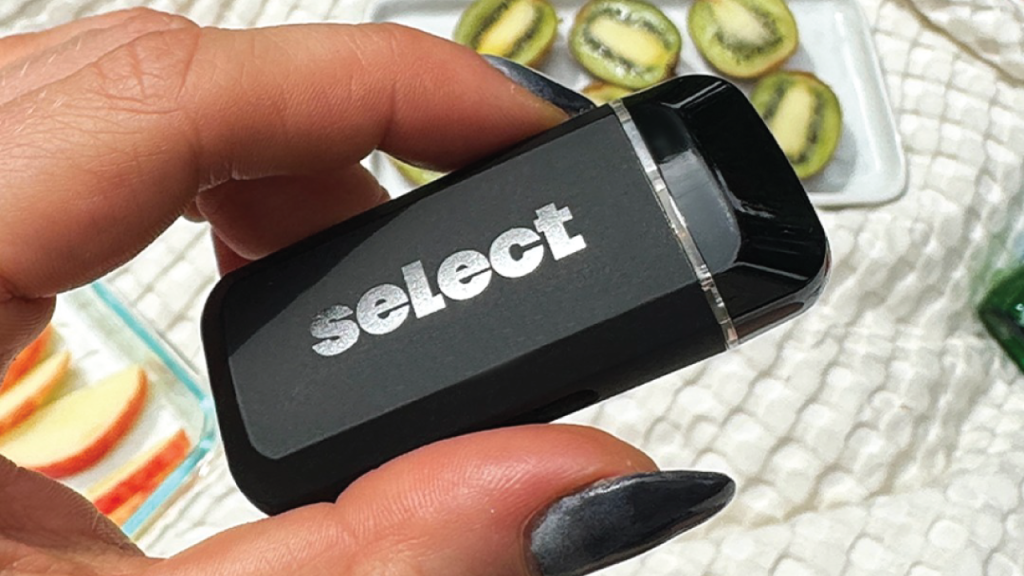 Close-up of Briq disposable vape device by Select, held in hand with fresh fruit slices in the background.