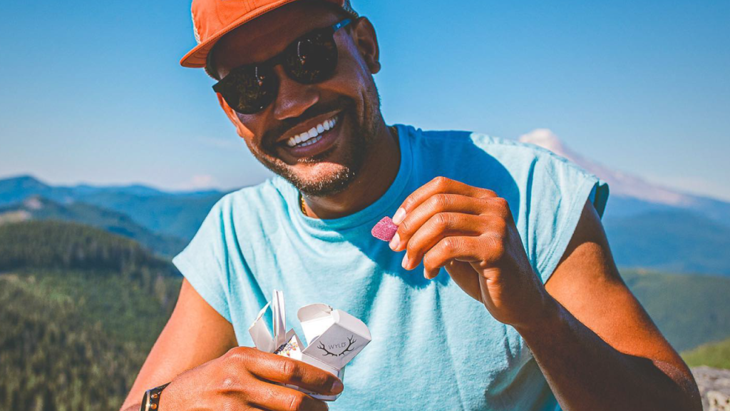 Man smiling while enjoying a Wyld cannabis gummy outdoors with mountains in the background