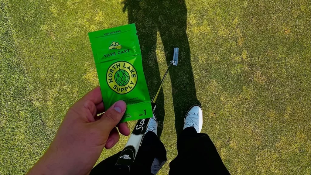 Hand holding a North Lake Supply 2g disposable cart vape on a golf green, showcasing on-the-go cannabis convenience.