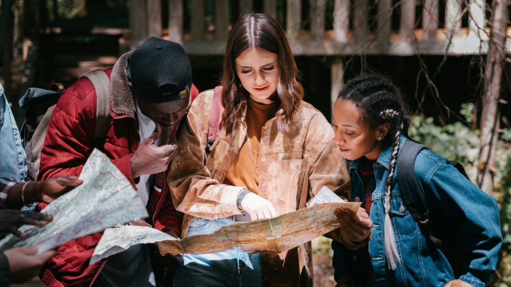 Group of young adults reading a map in a New Jersey forest, planning a cannabis-friendly fall foliage hike.
