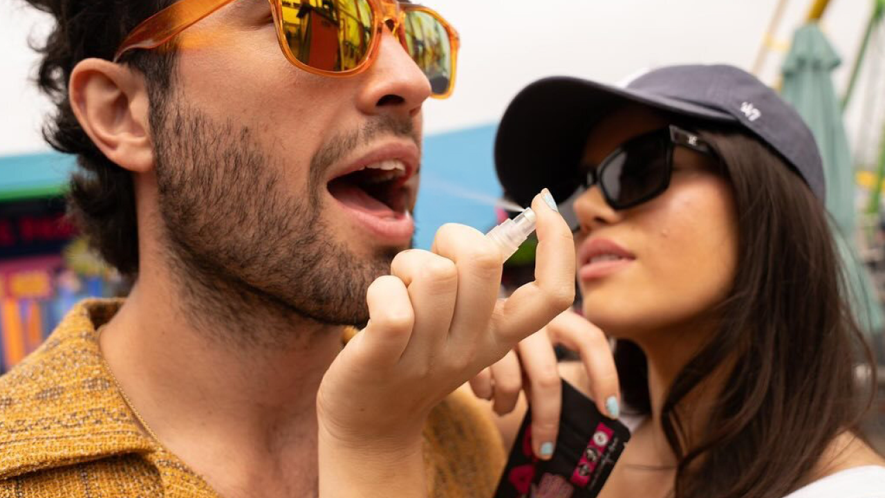 Woman holding a THC oral spray bottle up to a man’s mouth in an outdoor setting, demonstrating discreet cannabis use.
