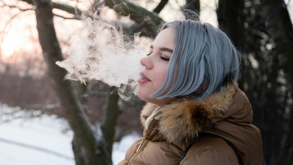 Woman exhales cannabis vapor outdoors in winter, embracing Dry January with a Cali sober lifestyle.