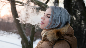 Woman exhales cannabis vapor outdoors in winter, embracing Dry January with a Cali sober lifestyle.