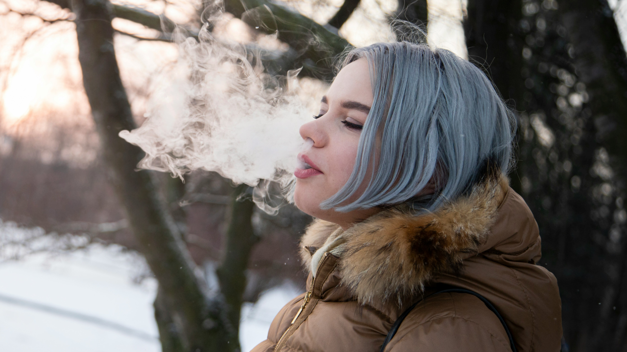 Woman exhales cannabis vapor outdoors in winter, embracing Dry January with a Cali sober lifestyle.